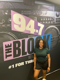 a woman standing in front of a sign that says 94 7 the block